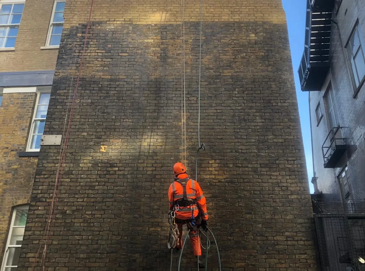 Rope access technicians carrying out professional brick facade cleaning, removing dirt, pollution, and stains to restore the building’s exterior.