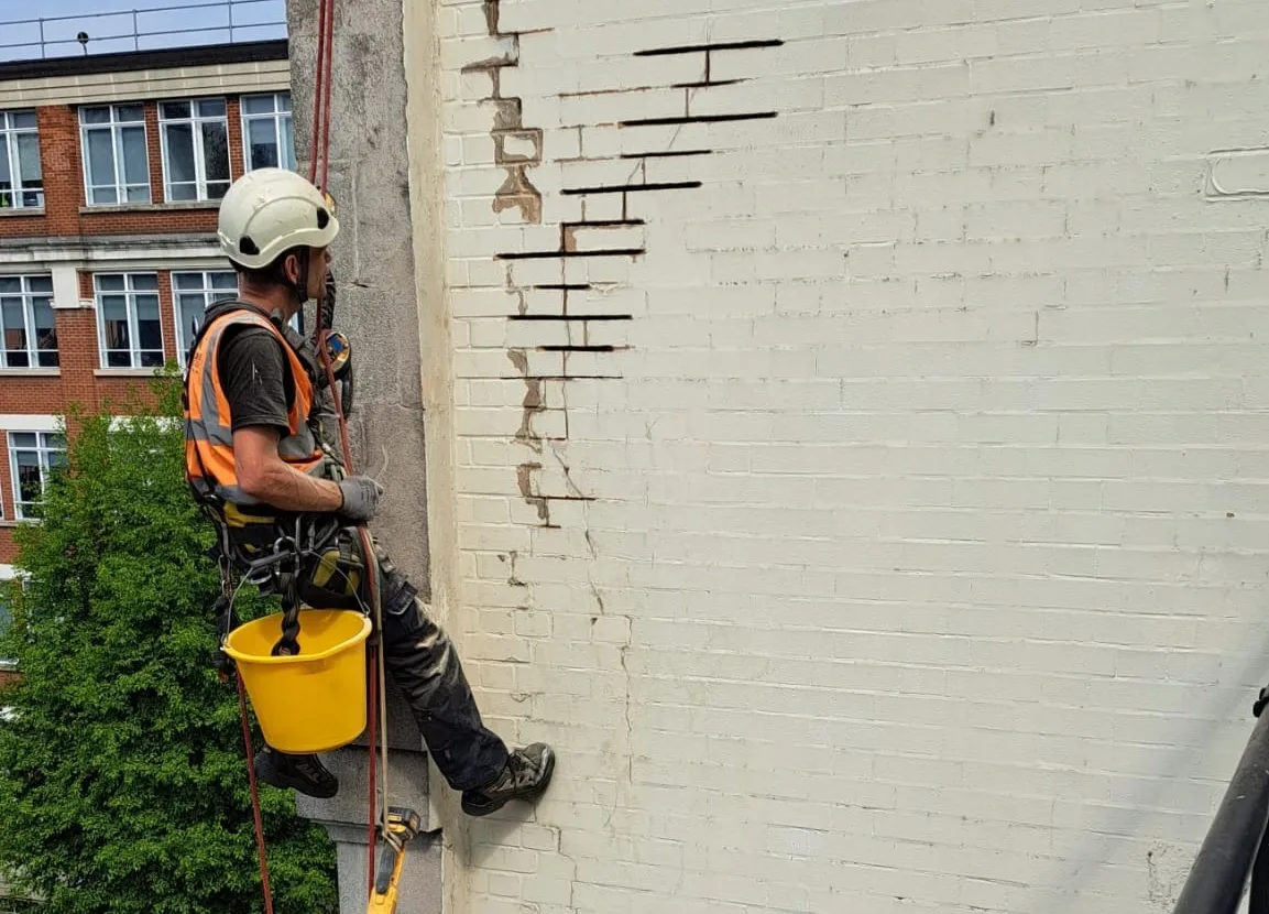 Rope access technician repairing a damaged brick facade in London.