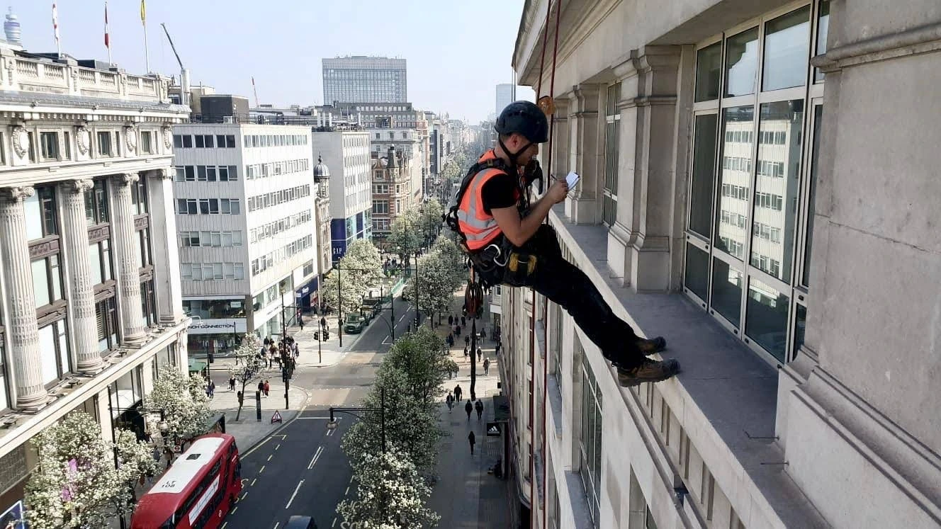 Rope access technician conducting a high-level building survey on a facade in London, inspecting exterior conditions.