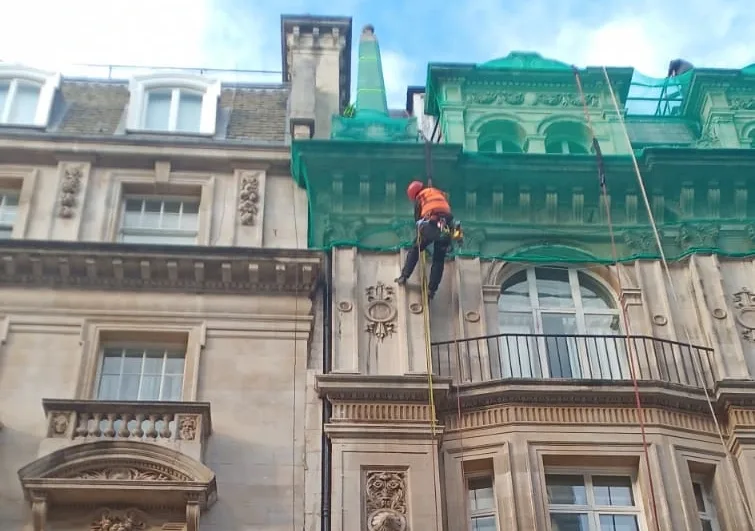 Rope access technician securing emergency netting on a historic building facade to prevent falling debris and ensure public safety.