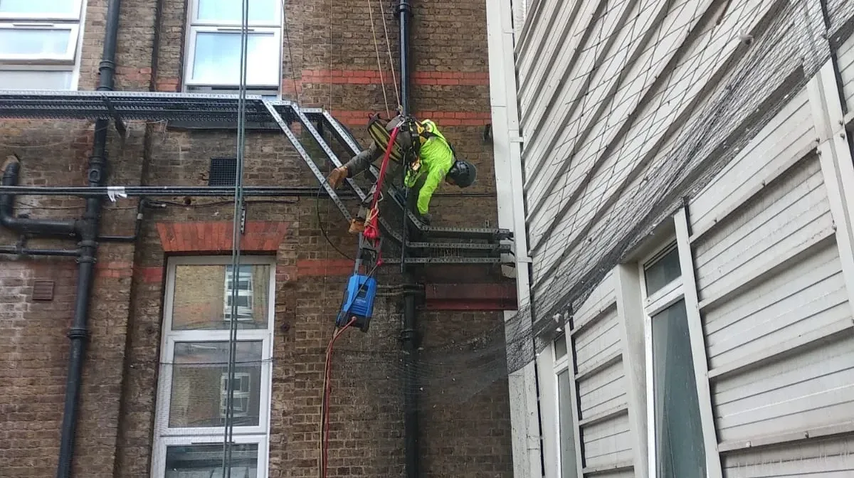 Rope access technicians carrying out facade cleaning on a high rise building in London to remove dirt grime and environmental buildup