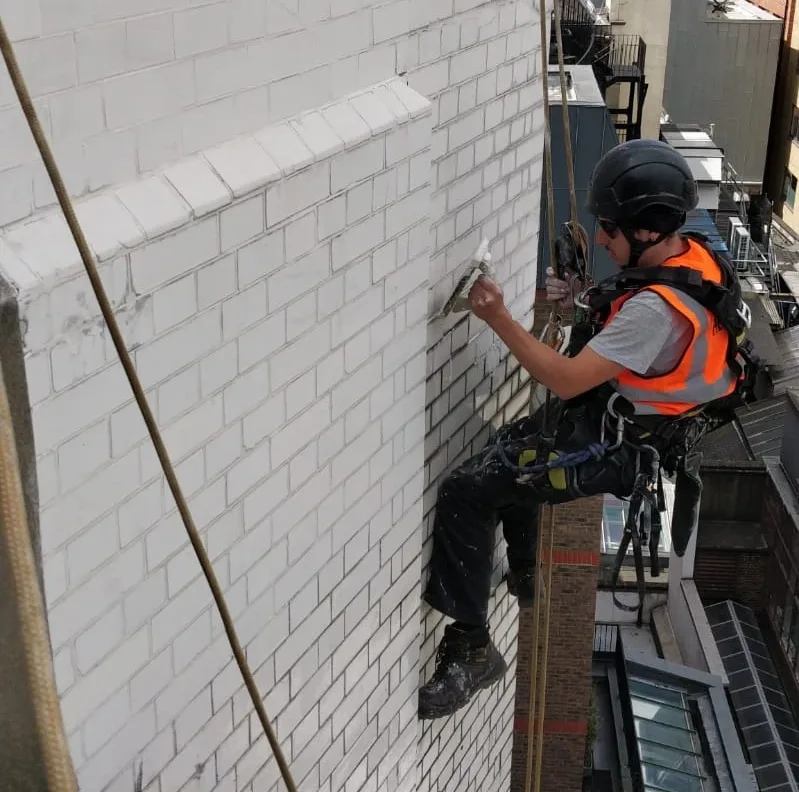 Rope access technicians applying waterproofing to glazed brick on a high rise building in London to protect against moisture and weather damage