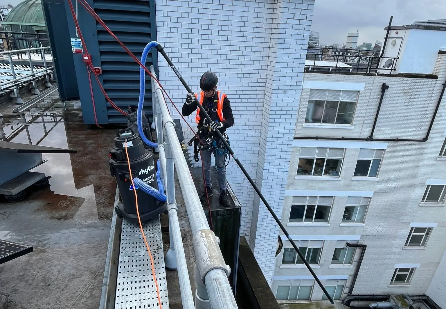 Rope access technicians carrying out gutter cleaning on a high rise building in London to remove debris and ensure proper water drainage