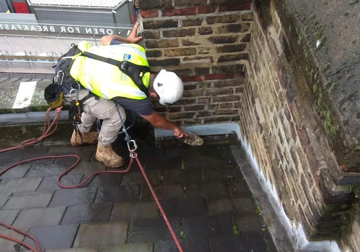 Rope access technicians removing muck from gutters on a high rise building in London to prevent blockages and ensure efficient drainage