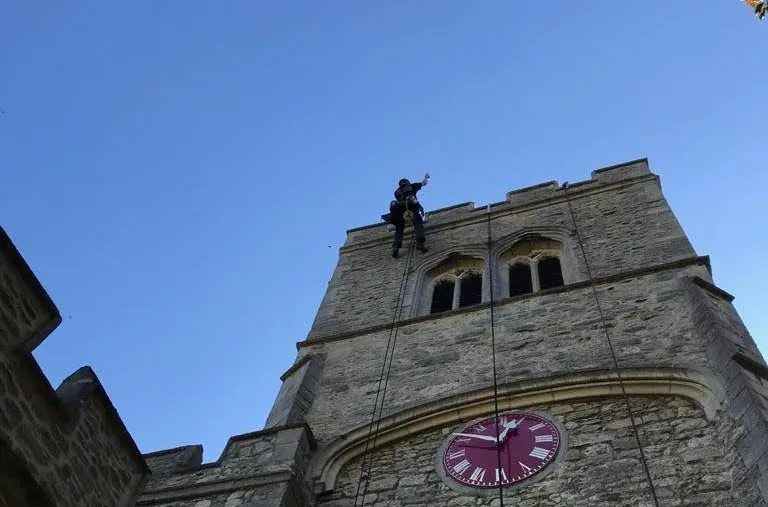 Rope access technicians installing a lightning protection system on a historic stone clock tower, ensuring safety and compliance with regulations.