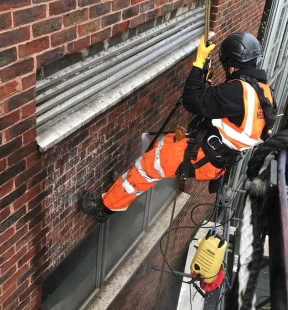 Rope access technicians performing pressure washing on a high rise building in London to remove dirt grime and stains