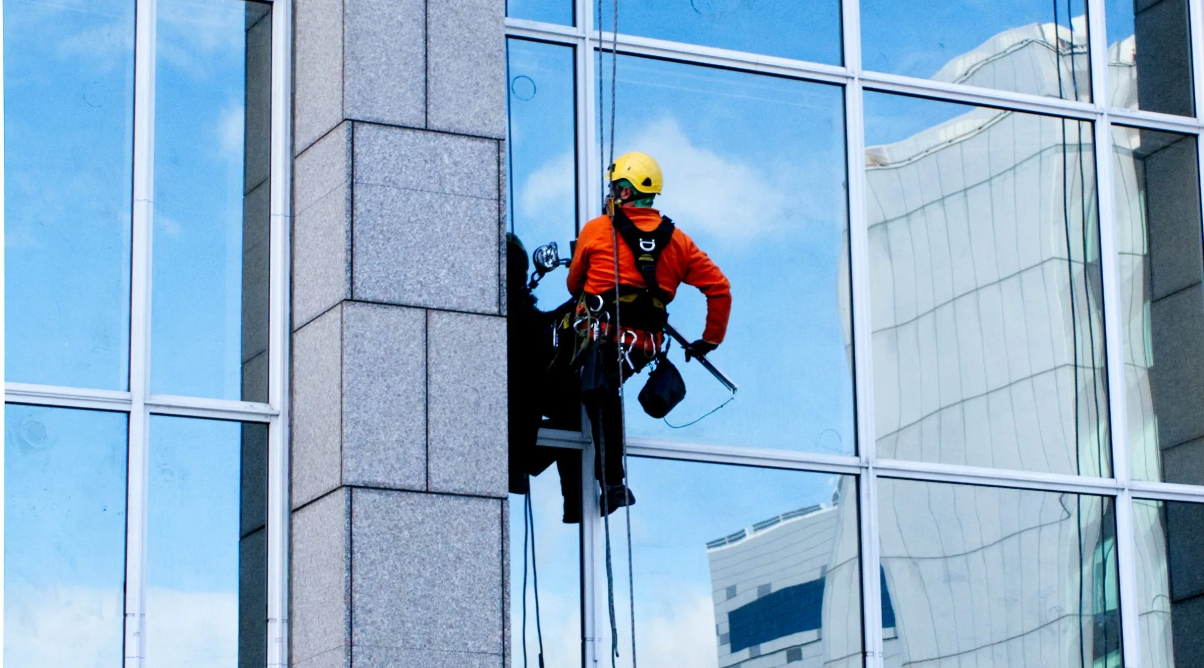 Rope access technician performing window glazing repair on a high-rise glass facade.