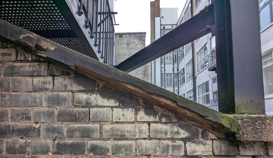 Close-up of a damaged coping stone on a brick parapet wall, showing cracks and weathering. Ideal for illustrating the need for coping stone repairs and waterproofing solutions.